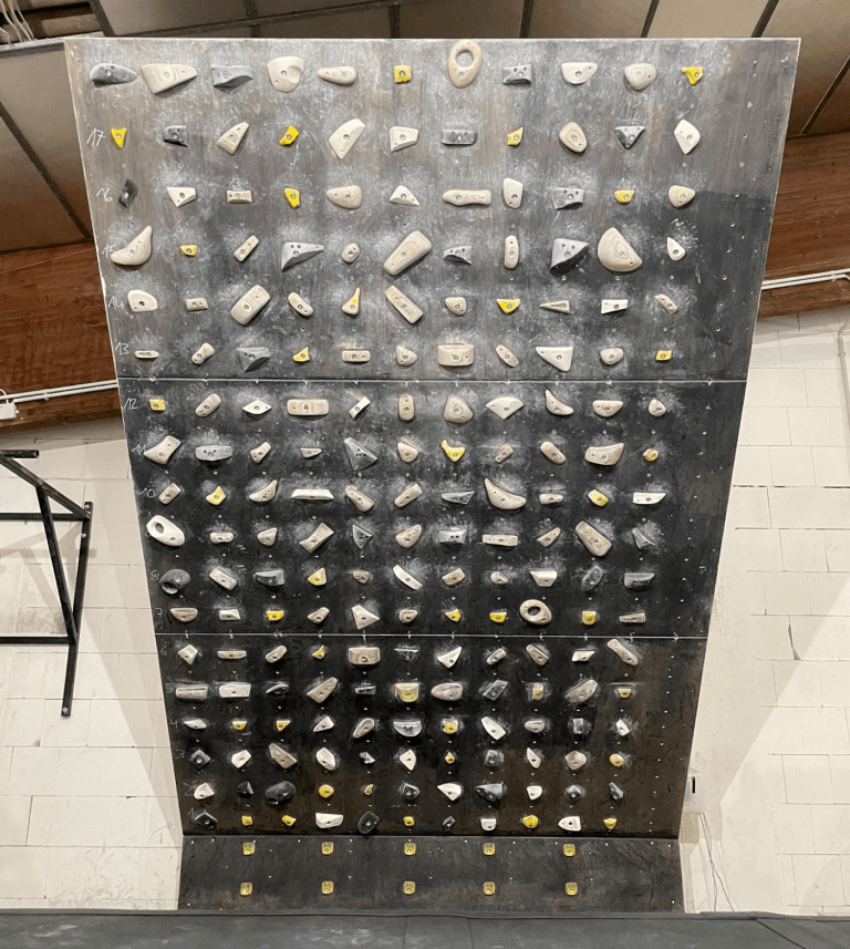 A black board with white and yellow holds against a white wall.