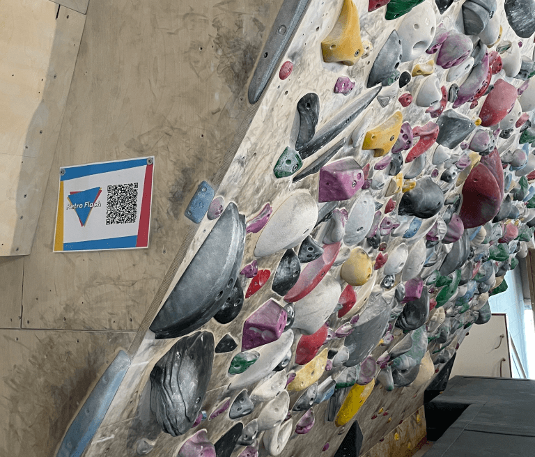 A laminated poster with a QR Code is posted on a climbing wall with different colored holds.