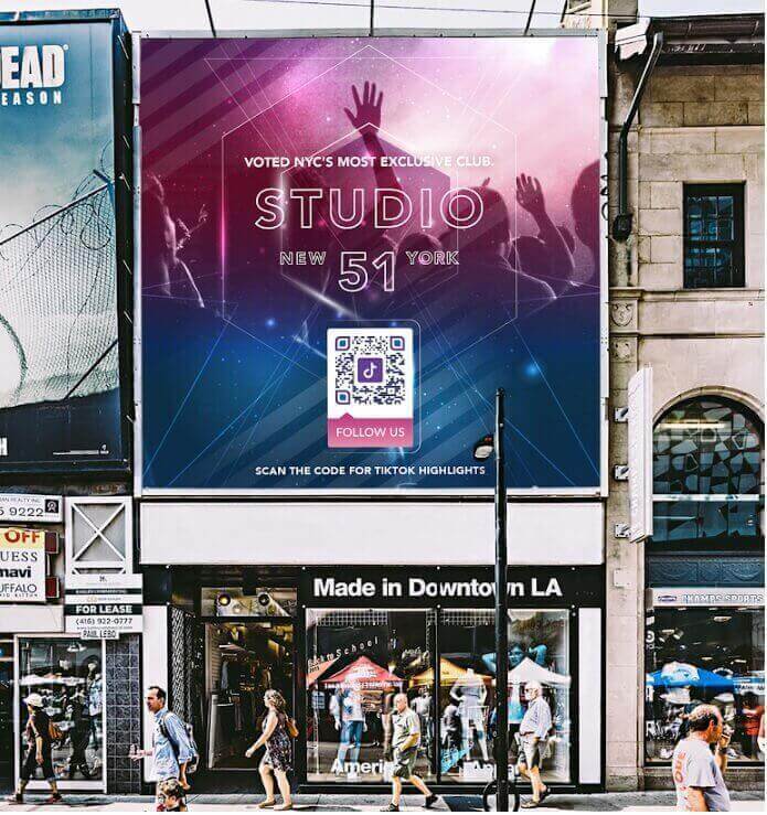 A view of a street with people walking by and a Studio 51’s billboard with a QR Code advertisement placed on it.