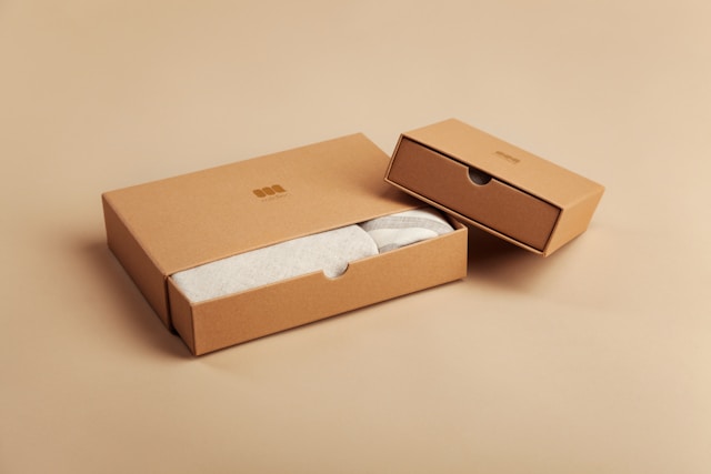 Two cardboard package boxes with a logo on top and gray clothing peeking out from the box.