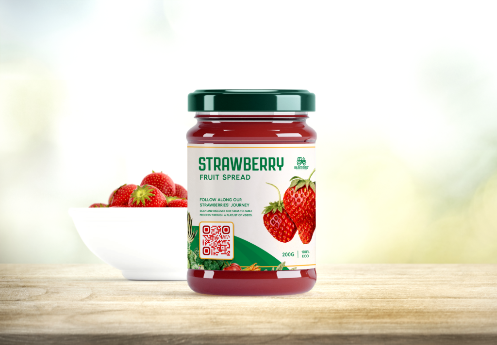 A jar of strawberry jam with a QR Code pasted on the label in front of a bowl of strawberries. 