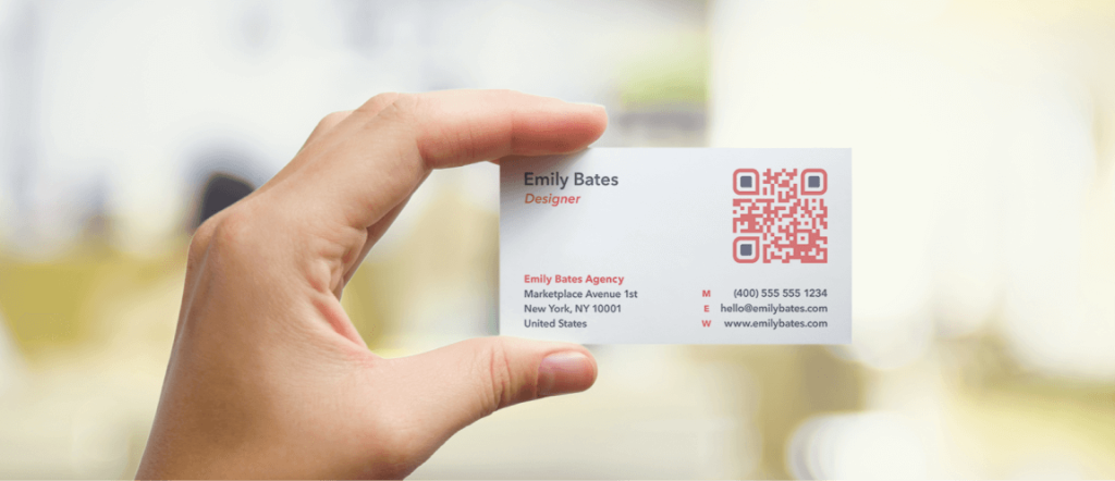 A hand holding a business card with a red and black QR Code printed on top of it.