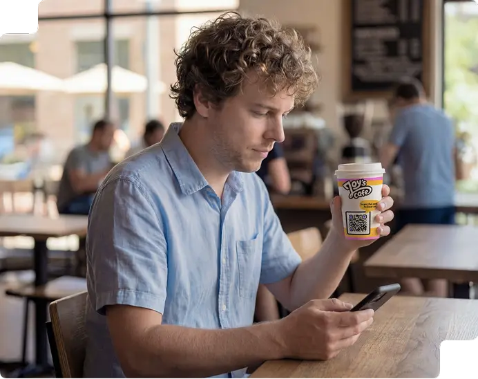 A person scanning a QR code on a coffee cup with their smartphone at a café